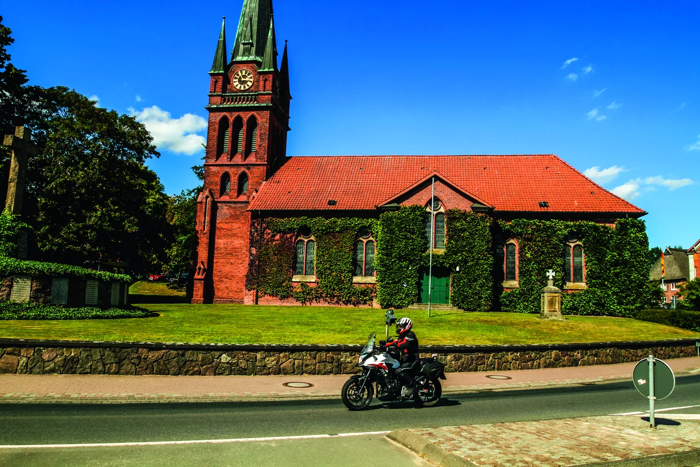 Backsteinkirche mit spitzem Turm, davor ein Motorrad